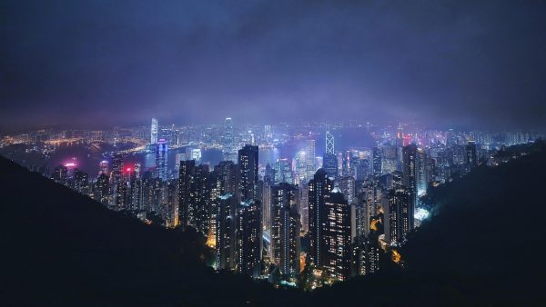 城市夜景中拍摄的旅行风景类快手 短视频 画面，霓虹倒映在湿润路面，行人撑伞走过，深紫粉色调